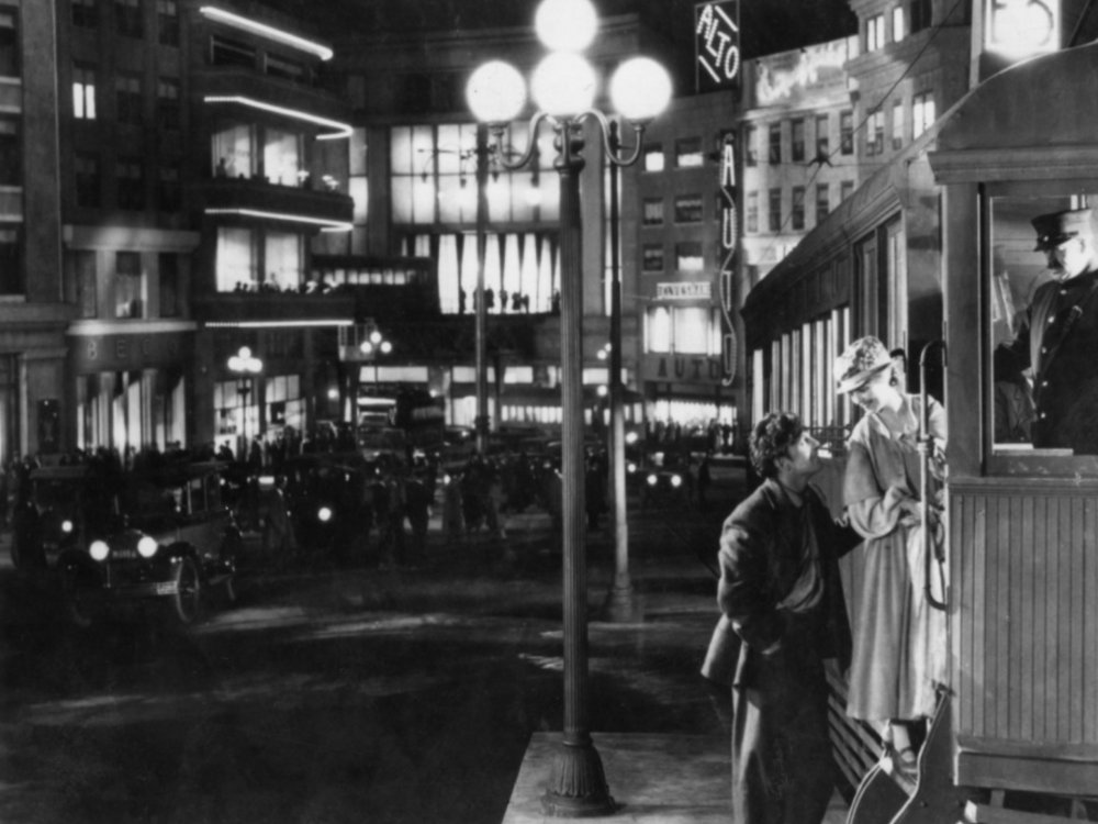Blick in eine nächtliche Stadt, am rechten Bildrand eine Tram. Eine Blonde Frau und ein Mann stehen sich vor ihr gegenüber