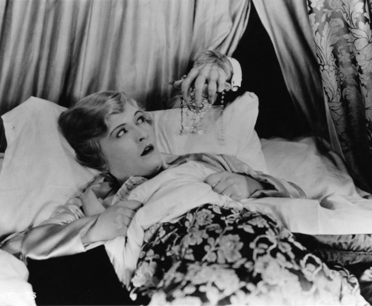 Eine blonde Frau liegt im Bett und guckt ängstlich. Von hinten greift die haarige Hand eines Monsters nach ihr